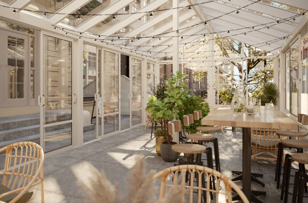 Interiörbild av ett fristående uterum med sadeltak från Expodul Uterum. Rummet används som restaurang och är trevligt inrett med matgrupper och gröna växter. Genom glaspartierna syns grönska och ett tegelhus.